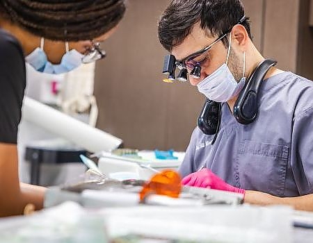 a man in a hospital mask is cutting a piece of paper  at cosmetic dentistry in Reston, VA